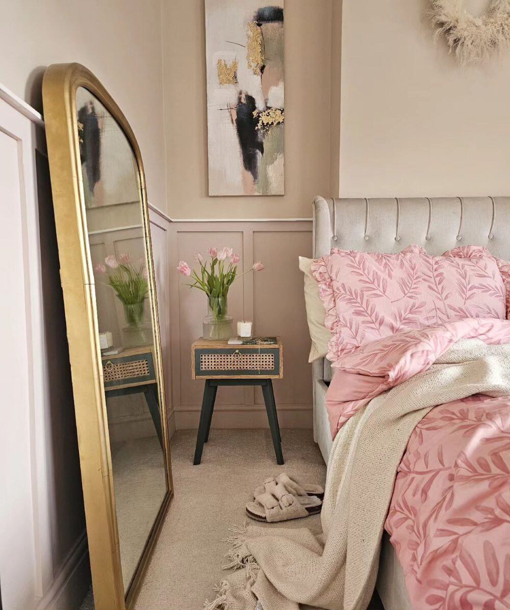 Stylish bedroom with grey bed, pink bedding and gold mirror