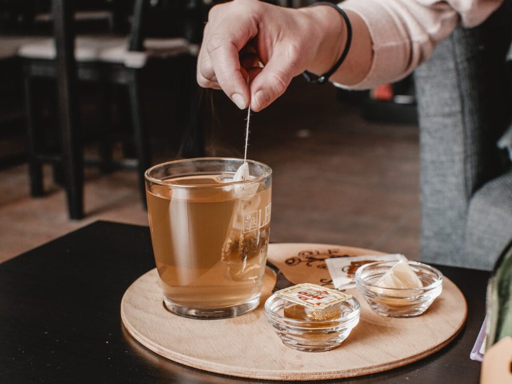 Person stirring herbal tea in a glass mug